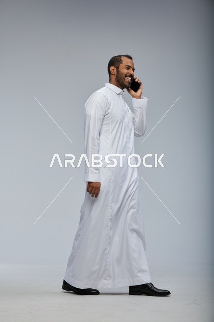 Saudi Man in White Thobe Talking on Smartphone