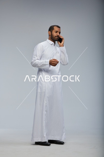 Saudi Man in White Thobe Talking on Smartphone