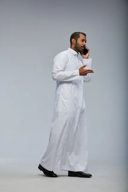 رجل سعودي بالثوب الأبيض يتحدث عبر الهاتف الذكي