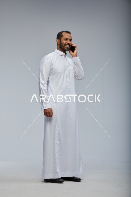 Saudi Man in White Thobe Talking on Smartphone