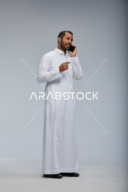Saudi Man in White Thobe Talking on Smartphone