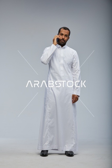 Saudi Man in White Thobe Talking on Smartphone