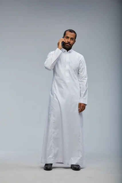 Saudi Man in White Thobe Talking on Smartphone