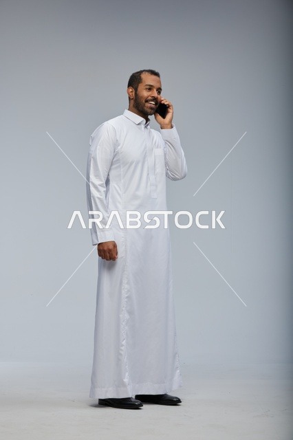 Saudi Man in White Thobe Talking on Smartphone