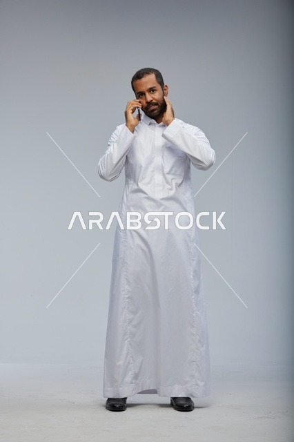 Saudi Man in White Thobe Talking on Smartphone