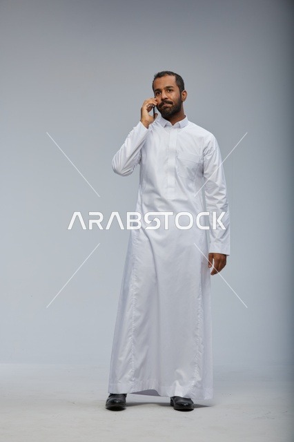 Saudi Man in White Thobe Talking on Smartphone