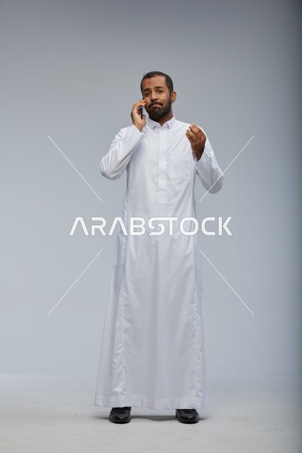 رجل سعودي بالثوب الأبيض يتحدث عبر الهاتف الذكي