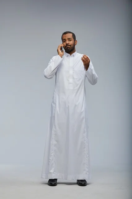 رجل سعودي بالثوب الأبيض يتحدث عبر الهاتف الذكي