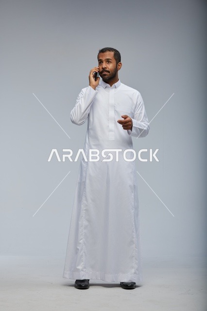 رجل سعودي بالثوب الأبيض يتحدث بالهاتف الذكي