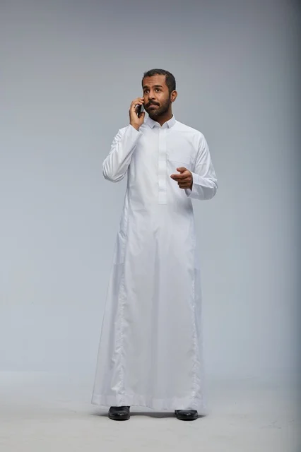 Saudi Man in White Thobe Talking on Smartphone