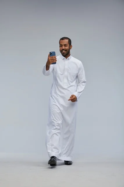 رجل سعودي بالثوب الأبيض يلتقط سيلفي بخلفية رمادية