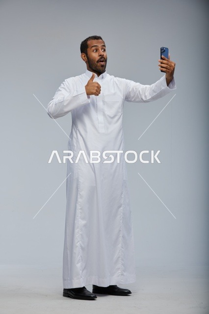 Saudi Man in White Thobe Taking Selfie with Smartphone