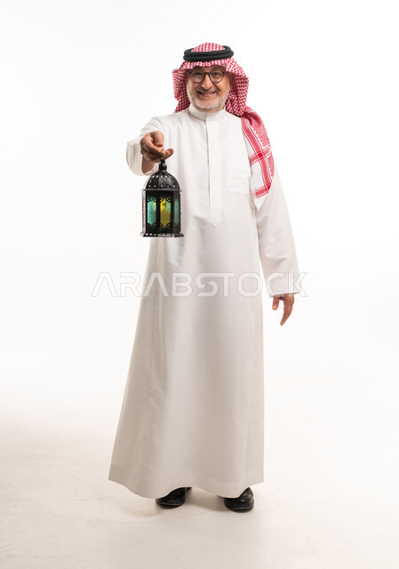 رجل سعودي مسن يحمل فانوس رمضان بخلفية بيضاء
