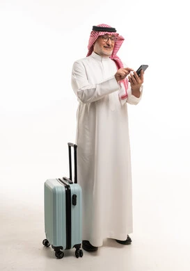 رجل سعودي مع حقيبة سفر يستخدم الهاتف الذكي