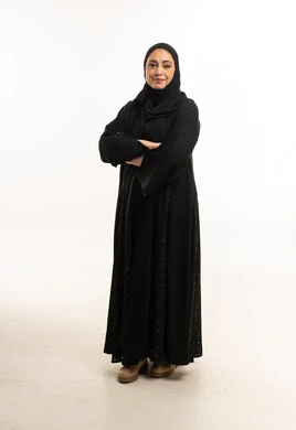 امرأة إماراتية بالعباءة السوداء أمام خلفية بيضاء