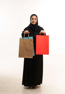 امرأة عربية بالعباءة تحمل أكياس التسوق