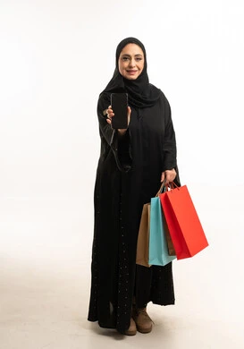 امرأة عربية بالعباءة مع حقائب تسوق وهاتف ذكي