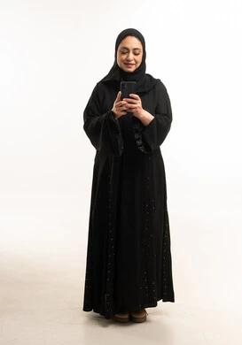 امرأة إماراتية بالعباءة السوداء تستخدم الهاتف الذكي