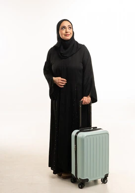 امرأة عربية بالعباءة السوداء تحمل حقيبة سفر