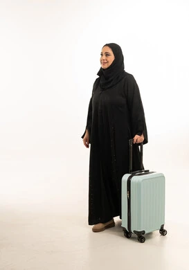 امرأة سعودية بالعباءة مع حقيبة سفر خلفية بيضاء