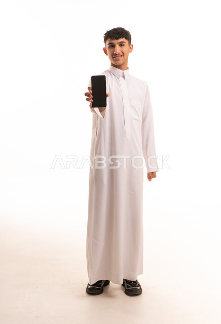 شاب سعودي بالثوب يحمل هاتف ذكي في الاستوديو