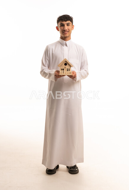 رجل سعودي بالثوب يحمل مجسم منزل خشبي