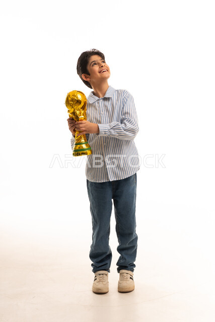 طفل سعودي يحمل مجسم كأس ذهبي بخلفية بيضاء