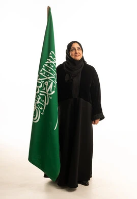 امرأة سعودية بالعباءة تقف مع العلم الوطني السعودي