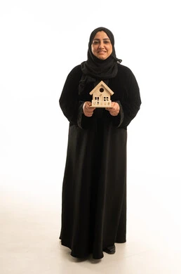 امرأة سعودية تحمل مجسم منزل خشبي خلفية بيضاء