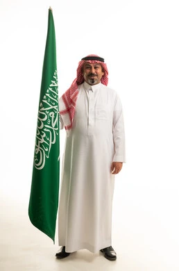 رجل سعودي بالزي التقليدي مع العلم الوطني