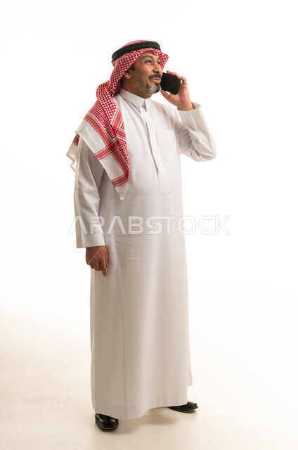 رجل سعودي بالثوب التقليدي يتحدث في الهاتف المحمول بالاستوديو