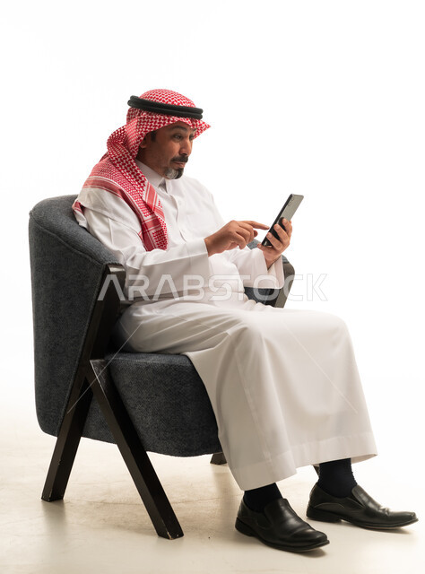 رجل سعودي بالزي التقليدي يستخدم الجوال على الكرسي