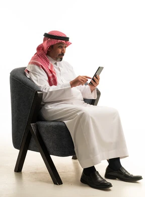 رجل سعودي بالزي التقليدي يستخدم الجوال على الكرسي