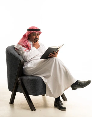 رجل سعودي بالثوب يقرأ كتاباً في الاستوديو على خلفية بيضاء