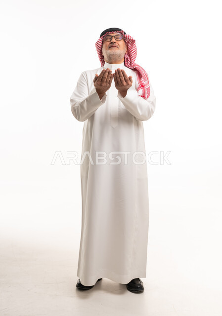 رجل سعودي بالزي التقليدي يرفع يديه بالدعاء خلفية بيضاء