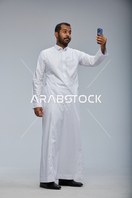 رجل سعودي بالثوب الأبيض يلتقط سيلفي بالهاتف الذكي
