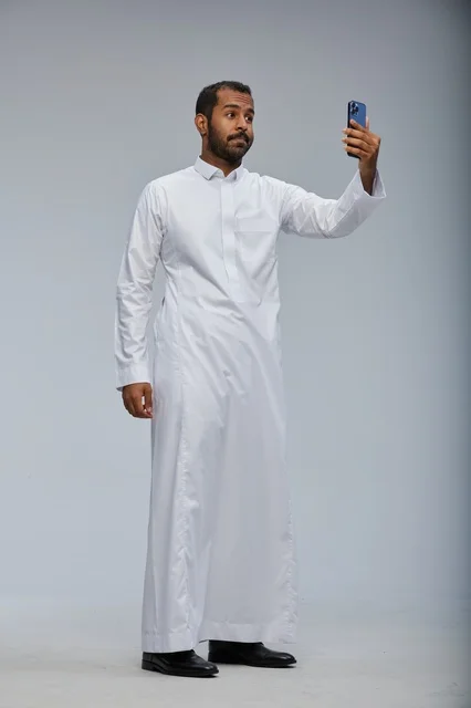رجل سعودي بالثوب الأبيض يلتقط سيلفي بالهاتف الذكي