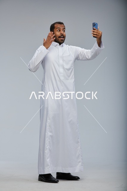 رجل سعودي بالثوب الأبيض يلتقط سيلفي بالهاتف الذكي