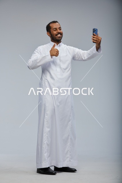 رجل سعودي بالثوب الأبيض يلتقط سيلفي بالهاتف الذكي