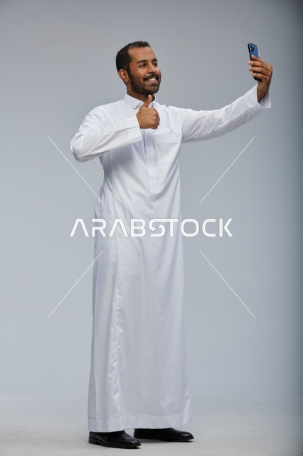رجل سعودي بالثوب الأبيض يلتقط سيلفي بالهاتف الذكي