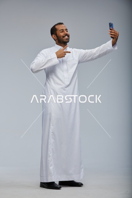 رجل سعودي بثوب أبيض يلتقط صورة سيلفي بهاتف ذكي