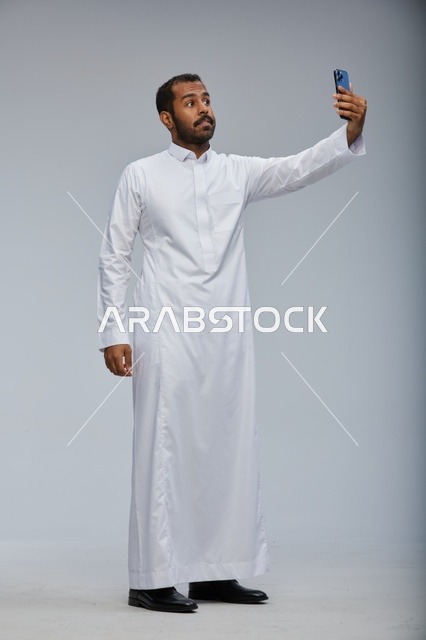 رجل سعودي بالثوب الأبيض يلتقط صورة سيلفي بهاتف ذكي
