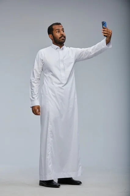 رجل سعودي بالثوب الأبيض يلتقط صورة سيلفي بهاتف ذكي