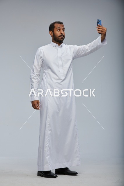 رجل سعودي بالثوب الأبيض يلتقط صورة سيلفي بالجوال استوديو