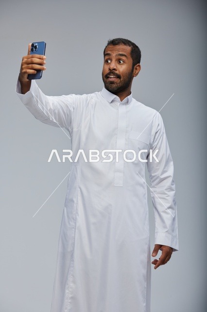 رجل سعودي بالثوب الأبيض يلتقط صورة سيلفي بالهاتف