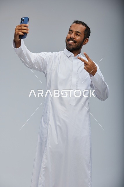 رجل سعودي بالثوب الأبيض يلتقط صورة سيلفي بالجوال