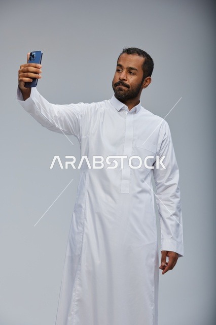 رجل سعودي بالثوب الأبيض يلتقط سيلفي بالجوال
