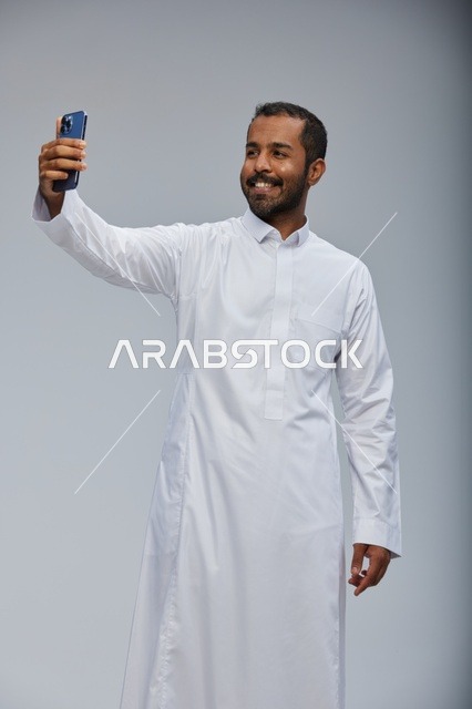 رجل سعودي بالثوب الأبيض يلتقط سيلفي بالهاتف الذكي