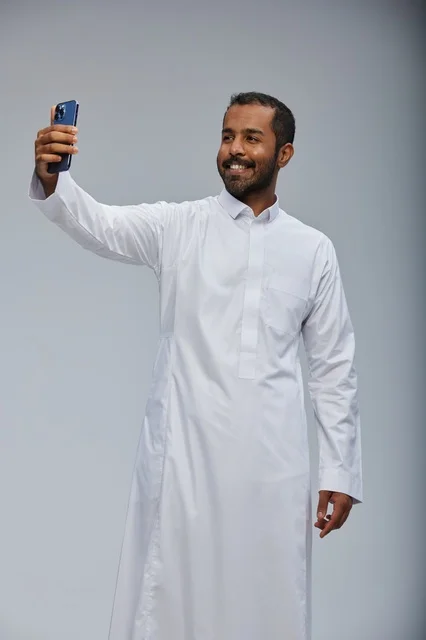 رجل سعودي بالثوب الأبيض يلتقط سيلفي بالهاتف الذكي