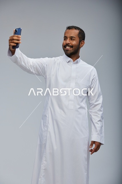 رجل سعودي بالثوب الأبيض يلتقط سيلفي بالهاتف الذكي